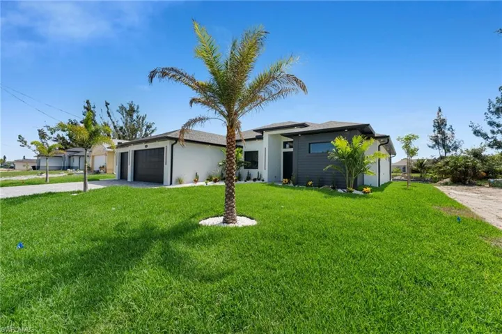 View of front of property featuring a garage, driveway, a front yard, and stucco siding