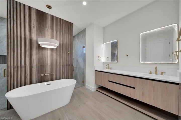 Full bathroom with a stall shower, wood finished floors, double vanity, a freestanding bath, and baseboards
