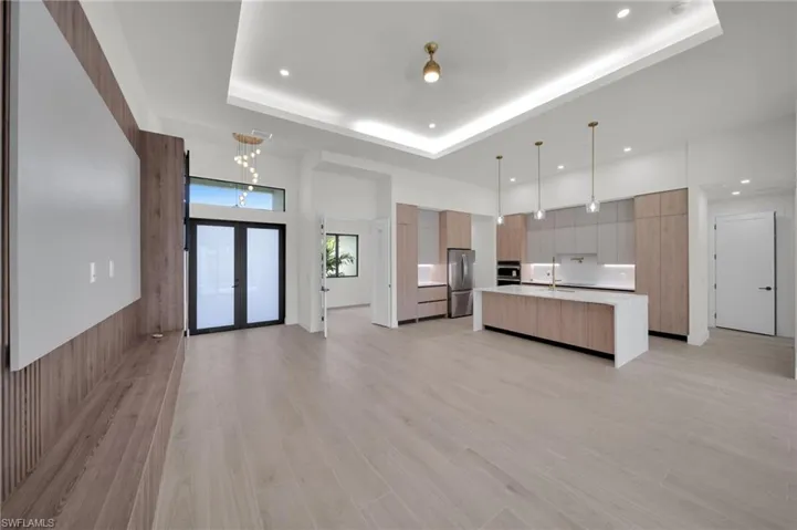 Kitchen featuring modern cabinets, stainless steel appliances, a raised ceiling, light countertops, and an island with sink