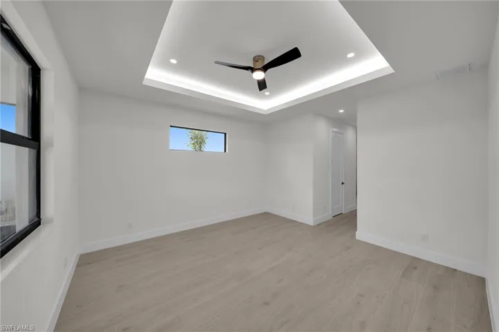 Empty room featuring recessed lighting, ceiling fan, a tray ceiling, light wood-style floors, and baseboards