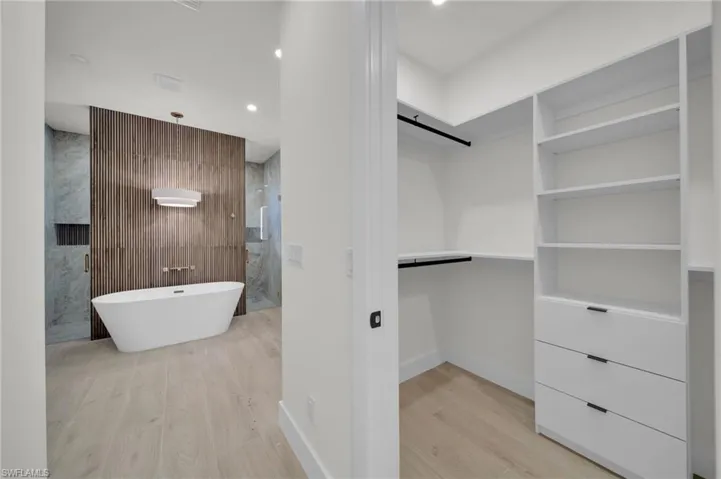 Bathroom featuring wood finished floors, a spacious closet, baseboards, walk in shower, and recessed lighting