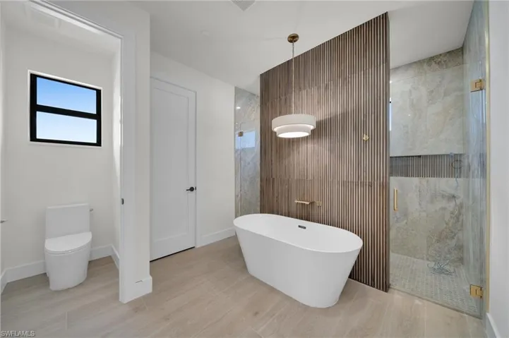Bathroom with a stall shower, wood finished floors, a freestanding bath, and toilet