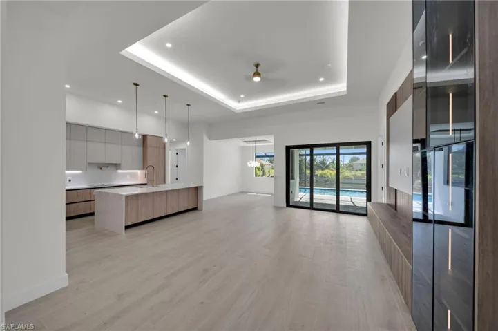 Unfurnished living room featuring a raised ceiling, recessed lighting, light wood-style flooring, a sink, and baseboards