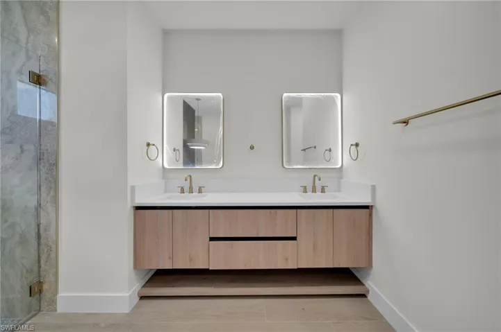 Full bathroom featuring baseboards, double vanity, and a shower stall