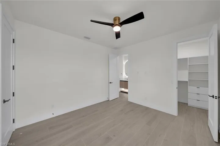 Unfurnished bedroom featuring light wood-type flooring, baseboards, a spacious closet, a ceiling fan, and a closet