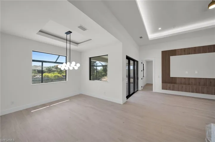 Spare room featuring a tray ceiling, light wood-type flooring, a chandelier, and baseboards