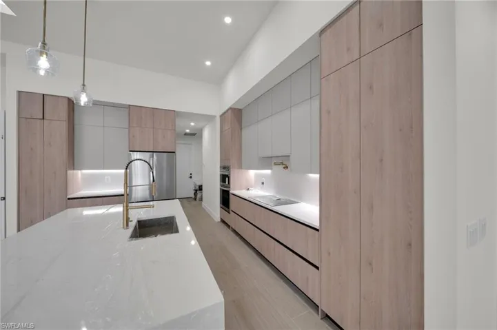 Kitchen with modern cabinets, a sink, light wood-style floors, light stone countertops, and hanging light fixtures