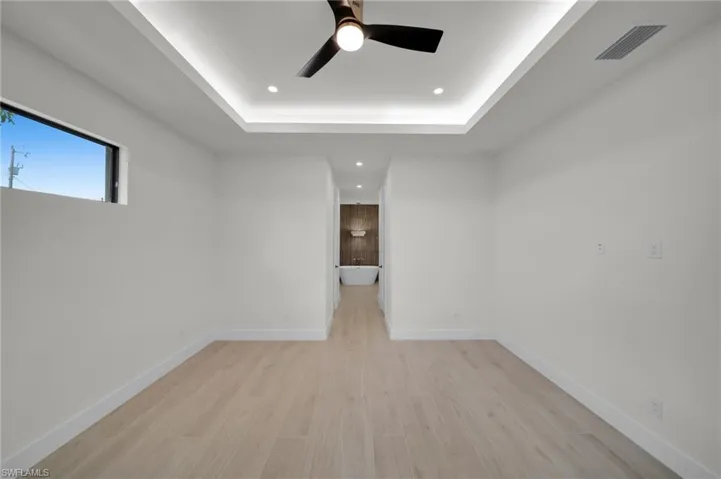 Unfurnished room featuring a raised ceiling, ceiling fan, recessed lighting, light wood finished floors, and baseboards