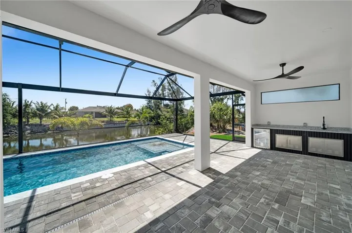 Outdoor pool featuring ceiling fan, an outdoor kitchen, a patio area, a water view, and a lanai
