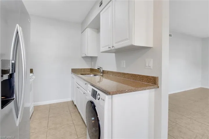 Kitchen with dark stone countertops, washer / dryer, stainless steel refrigerator with ice dispenser, white cabinetry, and a sink