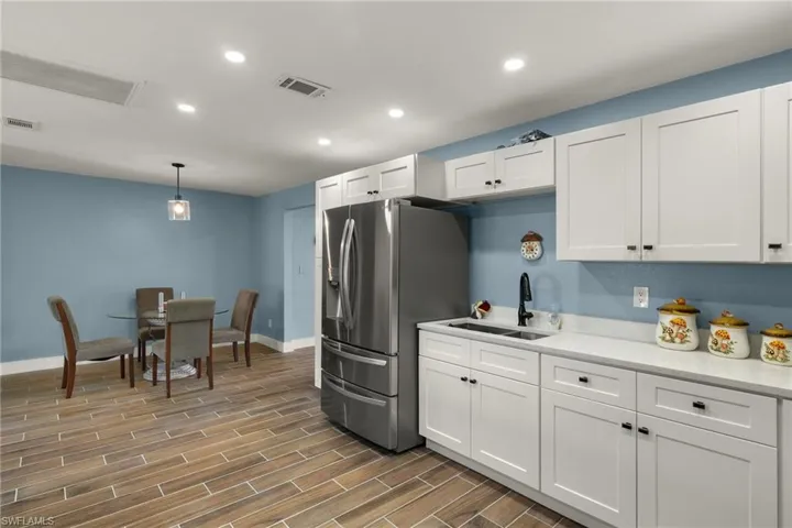 Kitchen with white cabinets, sink, stainless steel refrigerator with ice dispenser, and hanging light fixtures