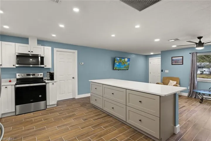 Kitchen with appliances with stainless steel finishes, gray cabinetry, ceiling fan, white cabinets, and a center island