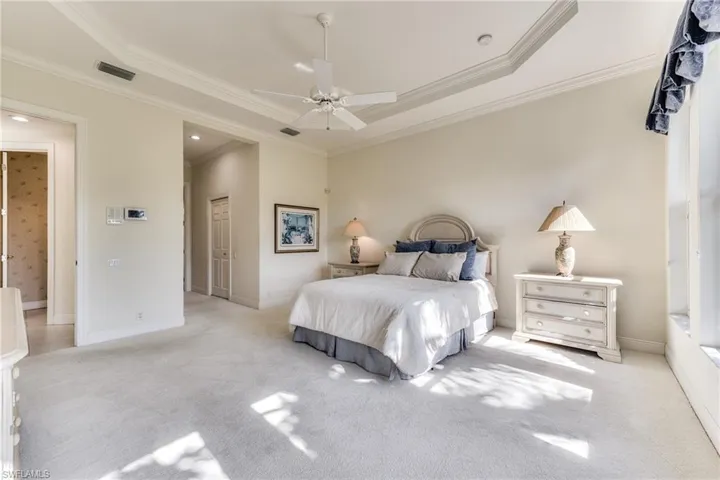 Carpeted bedroom with a tray ceiling, ceiling fan, and crown molding