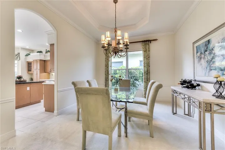 Large dining room with a tray ceiling, light carpet, a chandelier, and ornamental molding