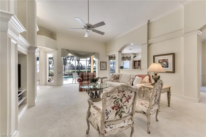 Carpeted living room with a high ceiling, ornate columns, ceiling fan, and ornamental molding