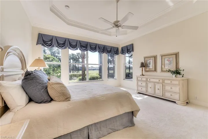 Carpeted bedroom featuring ceiling fan, a raised ceiling, crown molding, and multiple windows with gorgeous view