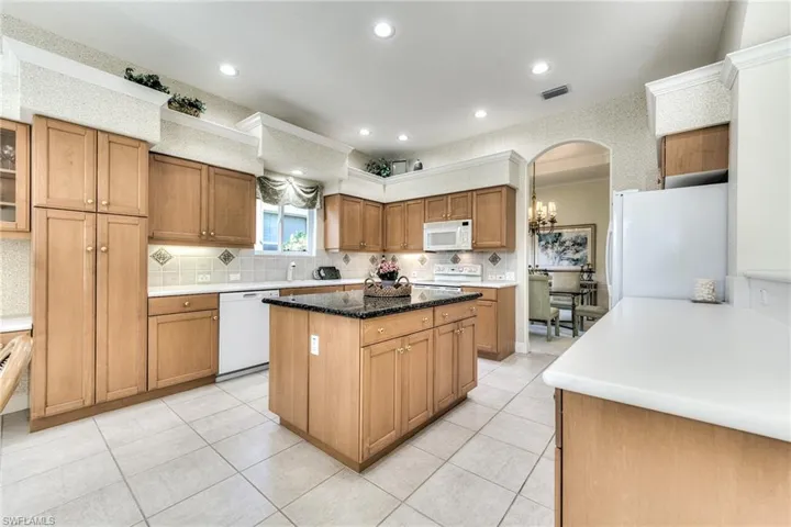 Kitchen featuring a center island, white appliances, backsplash and light tile flooring