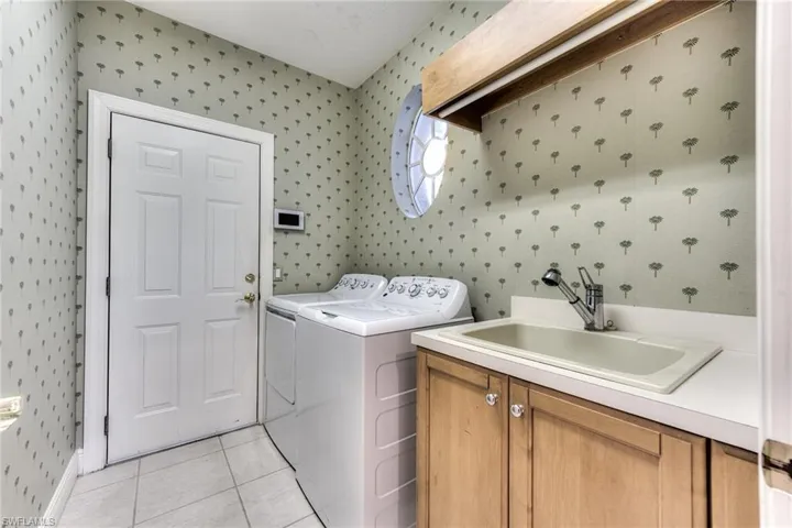 Laundry area featuring cabinets, washing machine and dryer, light tile tile floors, and sink