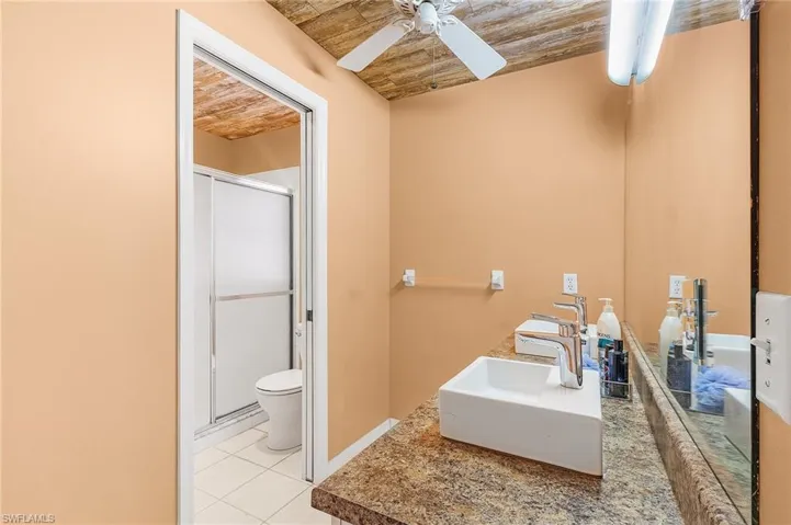 Bathroom with wood ceiling, tile patterned floors, ceiling fan, and toilet