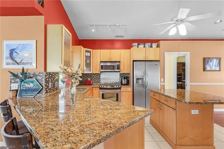 Kitchen with ceiling fan, tasteful backsplash, stainless steel appliances, kitchen peninsula, and a kitchen breakfast bar