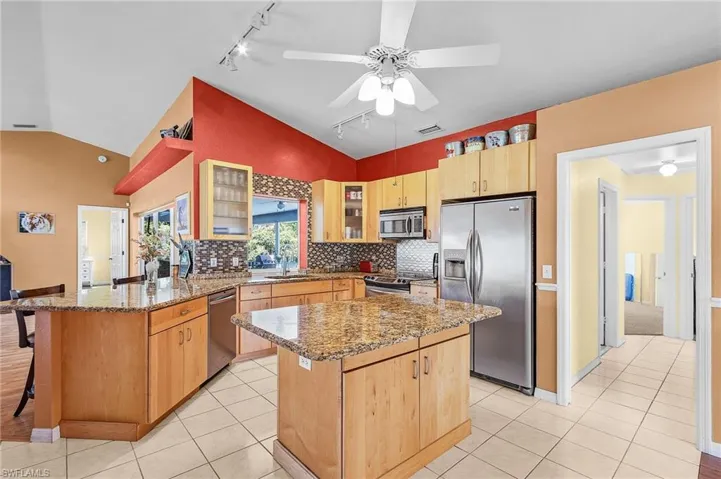 Kitchen featuring stainless steel appliances, a kitchen island, rail lighting, lofted ceiling, and ceiling fan