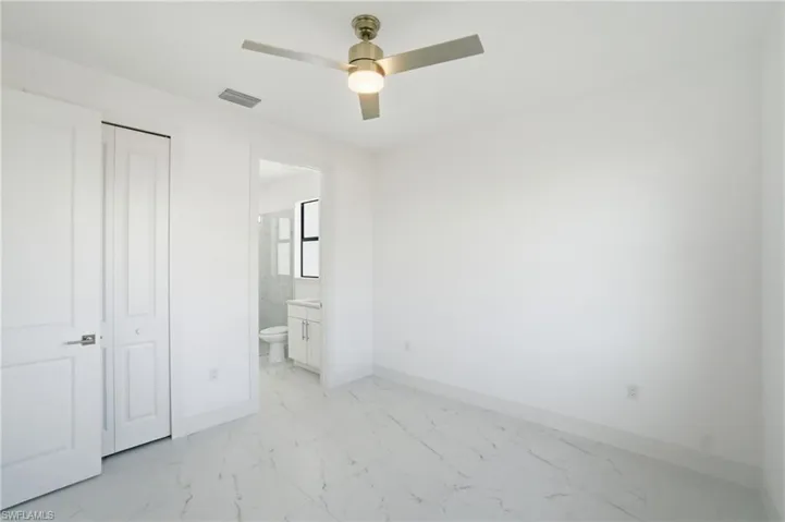 Unfurnished bedroom featuring light marble finish floors, a ceiling fan, connected bathroom, and a closet