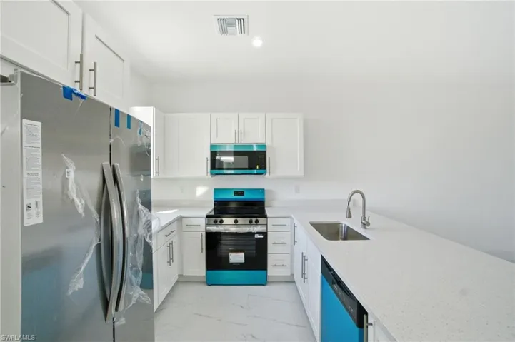 Kitchen with stainless steel appliances, white cabinets, light stone counters, and light marble finish flooring