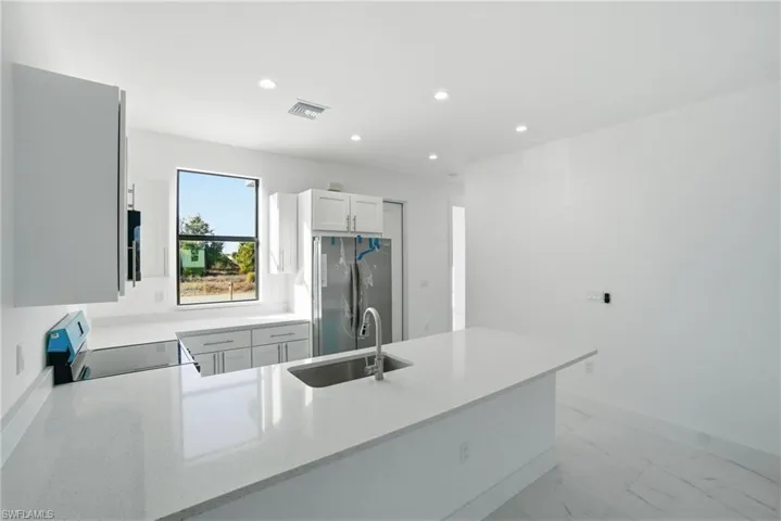 Kitchen with a peninsula, freestanding refrigerator, white cabinetry, light stone countertops, and recessed lighting
