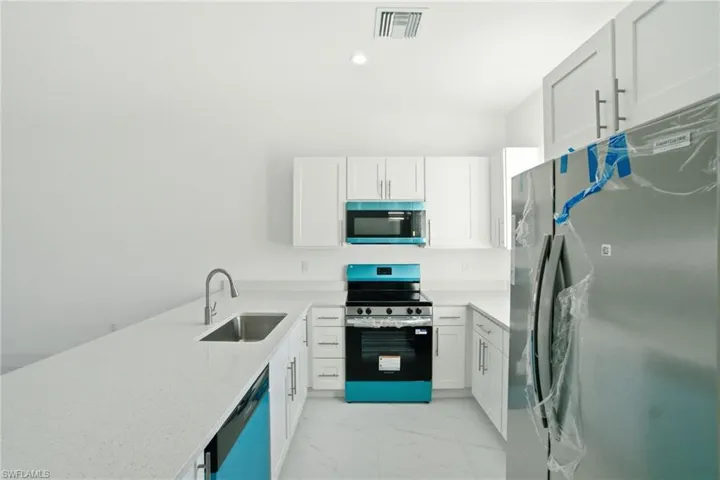 Kitchen featuring stainless steel appliances, light stone counters, light marble finish flooring, white cabinetry, and a peninsula