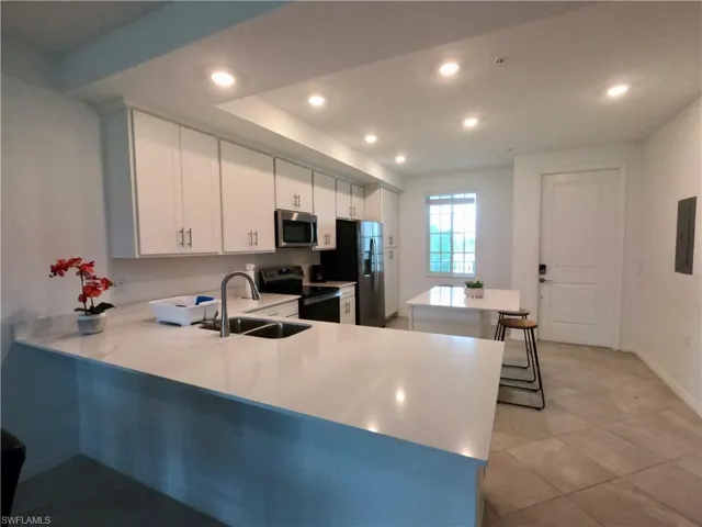 Kitchen with white cabinets, a peninsula, stainless steel appliances, recessed lighting, and a kitchen bar