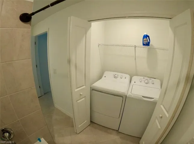 Washroom with light tile patterned floors and washing machine and dryer