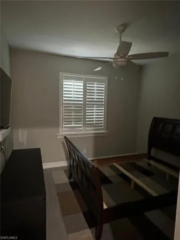Room featuring a window with white plantation shutters, a ceiling fan with integrated lighting, wood-finish flooring, and a baseboard trim