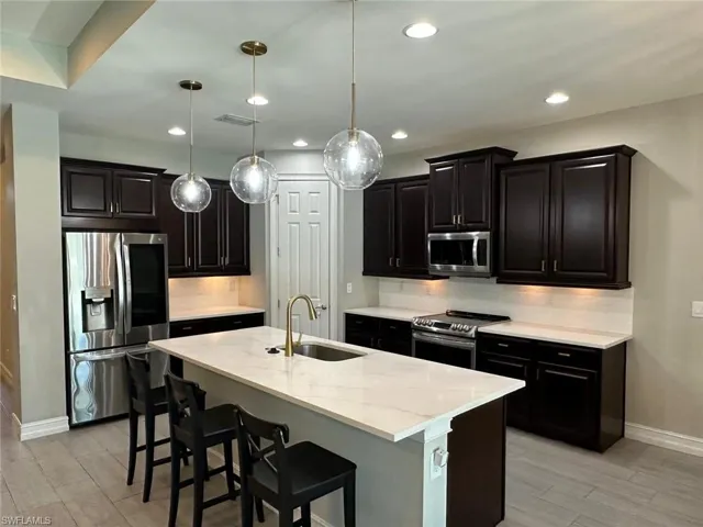 Modern kitchen featuring dark wood cabinetry, stainless steel appliances, a center island with seating, pendant lighting, and light-toned flooring