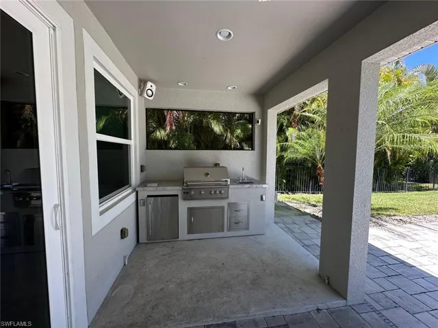 Outdoor kitchen featuring a built-in stainless steel grill, integrated sink, and under-counter refrigeration