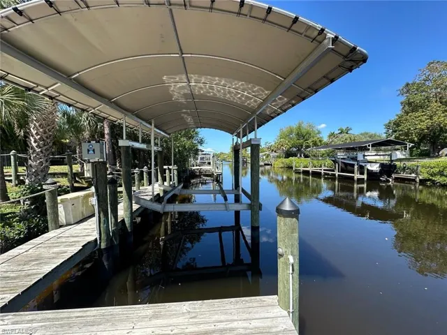 Covered boat dock with a wooden pier, featuring a boat lift structure and a tranquil canal setting