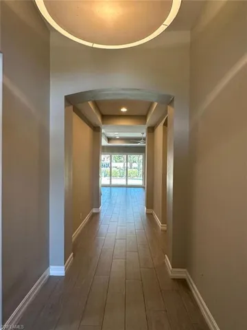 Entryway featuring wood-finish tile flooring, a circular ceiling light fixture, arched doorways, and tray ceilings