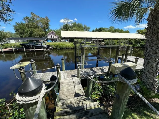 Private dock with a covered boat lift, featuring a wooden deck and pilings with rope accents