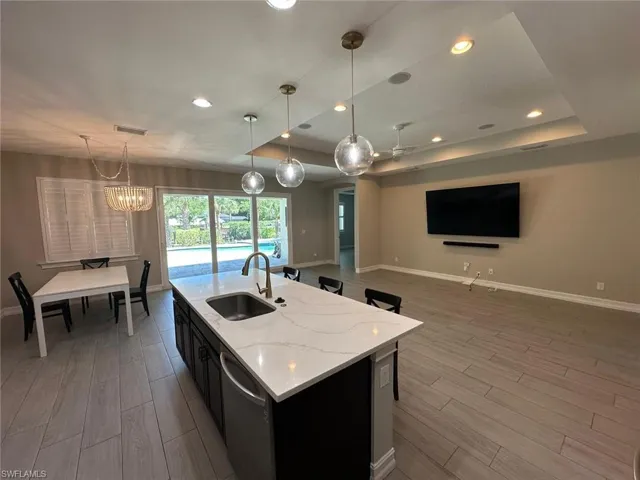 Spacious open-concept interior featuring a kitchen island with a white stone countertop and undermount sink, recessed lighting, and large sliding glass doors leading to an outdoor pool area