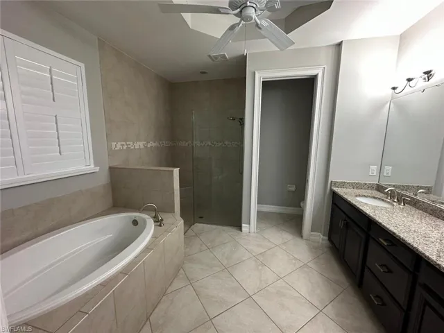 Spacious bathroom featuring a built-in soaking tub, glass-enclosed shower with tiled walls, and a dual vanity with a speckled countertop
