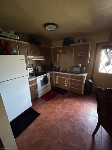 Kitchen featuring white appliances, sink, backsplash, and dark tile flooring