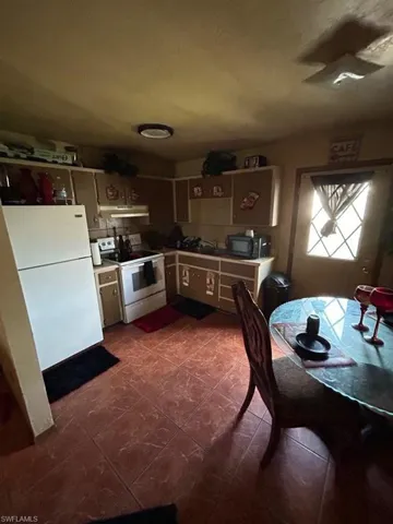 Kitchen with ventilation hood, dark tile floors, and white appliances