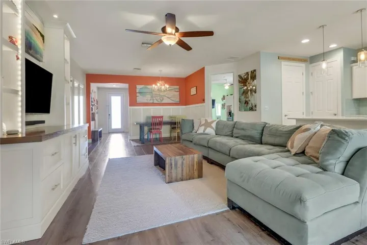 Living room featuring visible vents, wood finished floors, a wainscoted wall, ceiling fan with notable chandelier, and recessed lighting