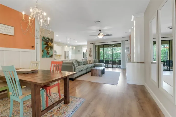 Dining room with plenty of natural light, light wood-style floors, ceiling fan with notable chandelier, and a wainscoted wall
