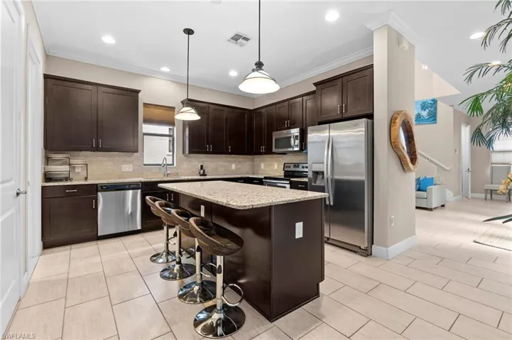 Kitchen with dark brown cabinetry, appliances with stainless steel finishes, a kitchen breakfast bar, decorative backsplash, and crown molding