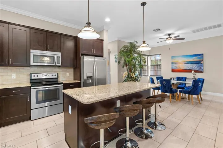 Kitchen with appliances with stainless steel finishes, dark brown cabinets, tasteful backsplash, decorative light fixtures, and crown molding