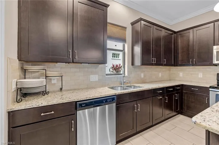 Kitchen featuring appliances with stainless steel finishes, dark brown cabinetry, light stone countertops, ornamental molding, and tasteful backsplash