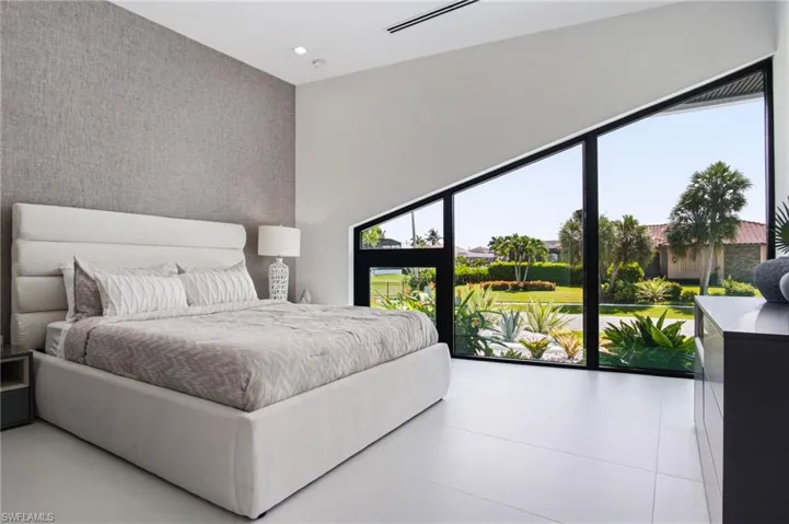 Expansive angled window wall with black framing, high ceilings with recessed lighting, textured accent wall, and large format light-toned floor tiles