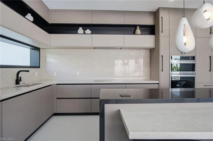 Modern kitchen featuring light-toned cabinetry with integrated hardware, a contrasting black accent shelf, and a light-colored countertop