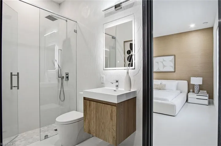 Bathroom featuring a frameless glass shower enclosure, a wall-mounted vanity with wood-finish cabinetry, an illuminated mirror, and hexagonal tile flooring