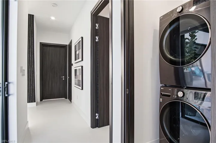 Integrated laundry area featuring a stacked washer and dryer, adjacent to a hallway with recessed lighting